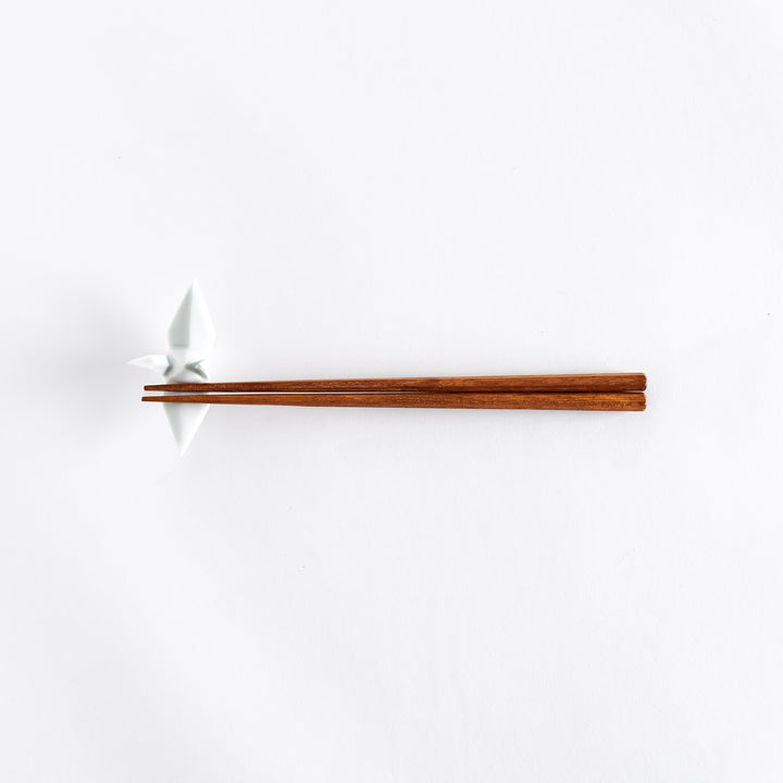 Wide view of chopsticks resting on the white ceramic crane-shaped chopstick rest.