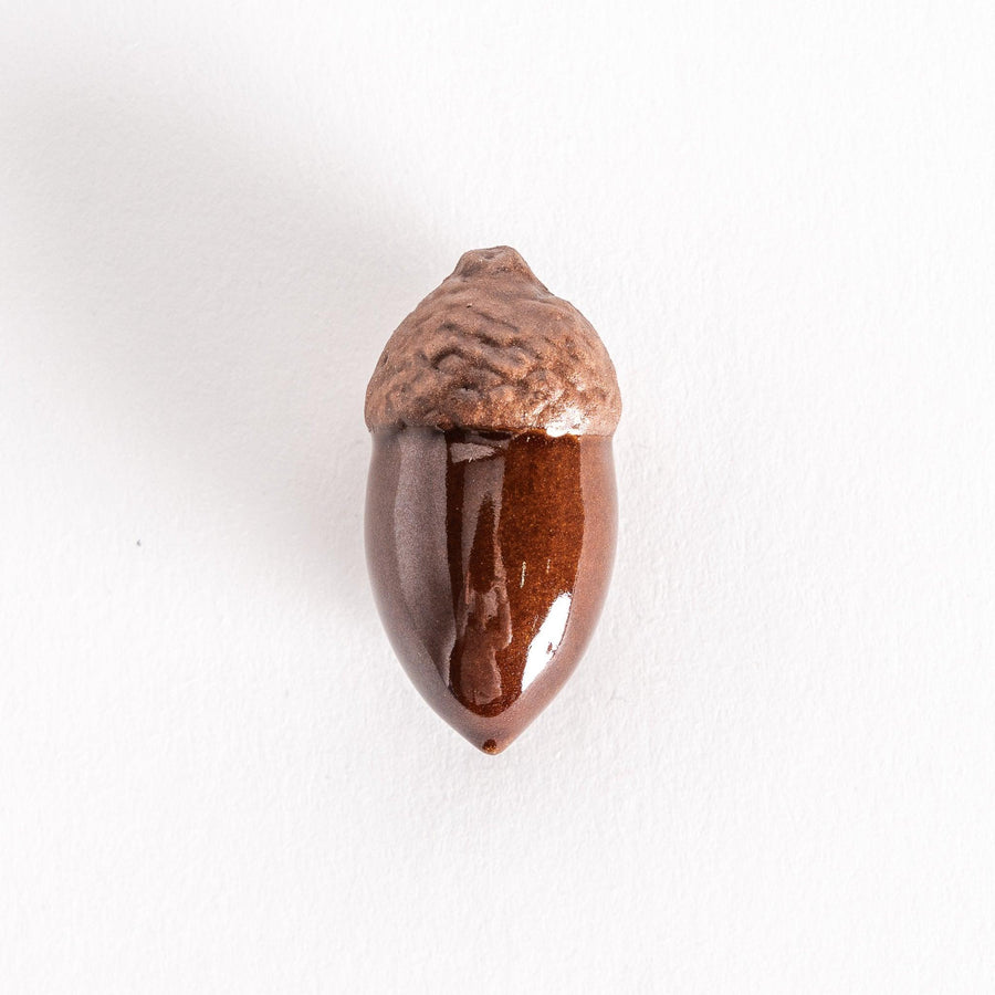 A ceramic chopstick rest shaped like an acorn with a glossy brown body and textured top on a white background.