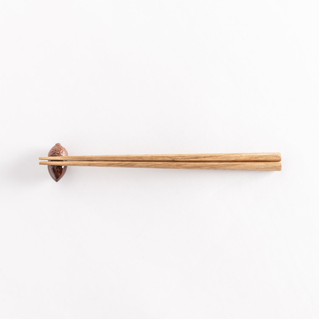 A wider view of the ceramic acorn chopstick rest with chopsticks placed on it, highlighting its elegant design on a white background.