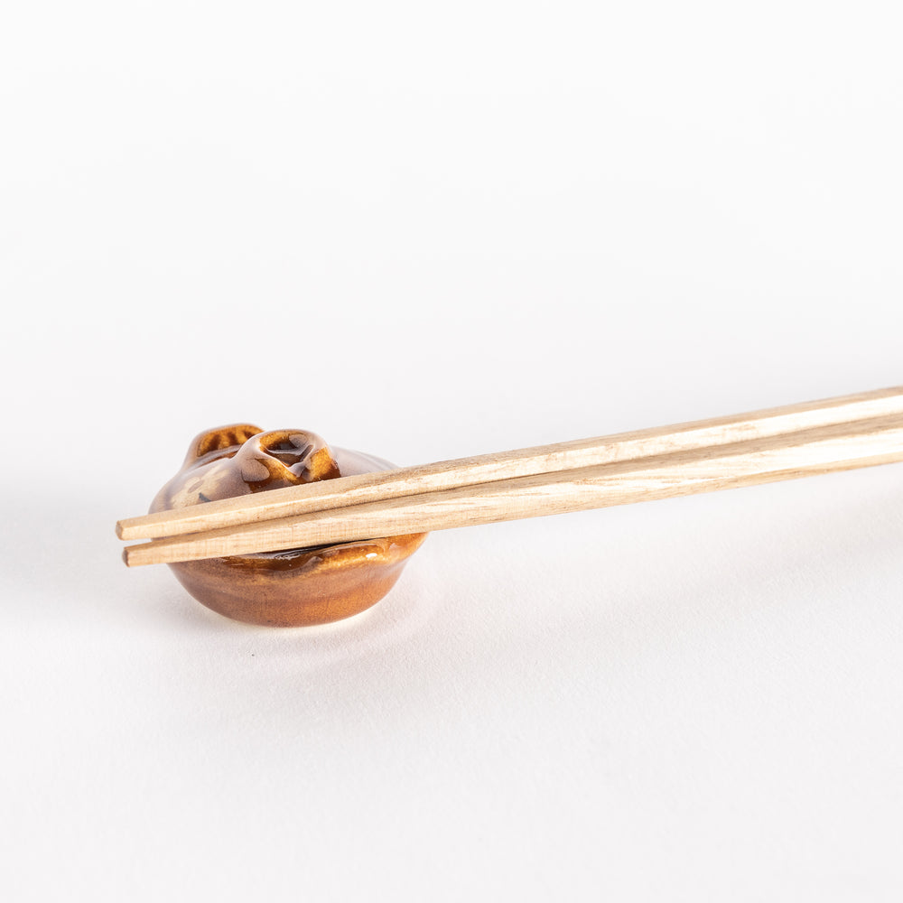 Close-up of the amber earthen pot chopsticks rest with chopsticks placed across its top.