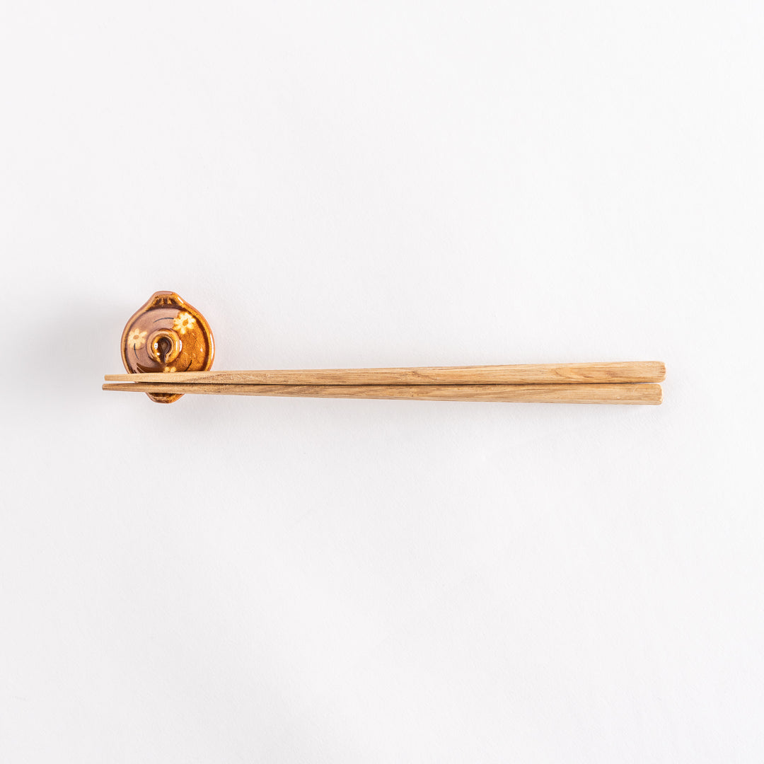 Full view of the amber earthen pot chopsticks rest with chopsticks resting horizontally.