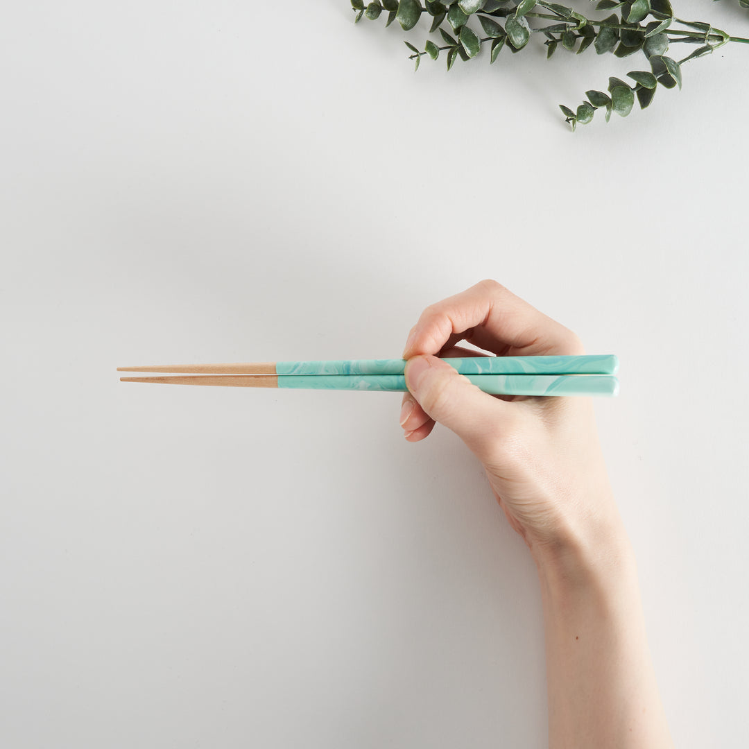 A pair of aqua chopsticks held in a hand, emphasizing the marbled design and their elegant look.