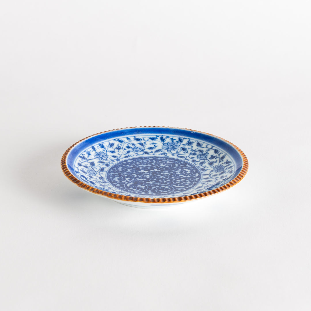 A ceramic plate with an intricate blue floral design centered around a bold circular pattern, framed by a copper-colored textured rim.