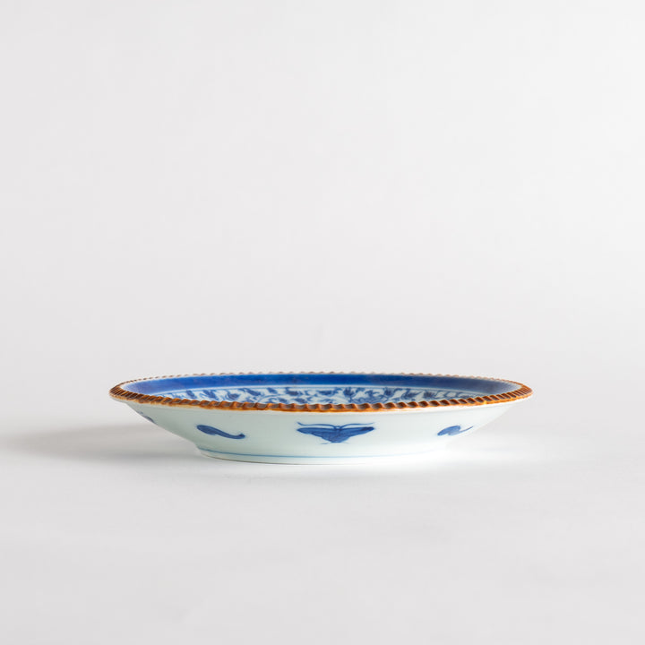 A ceramic plate with an intricate blue floral design centered around a bold circular pattern, framed by a copper-colored textured rim.