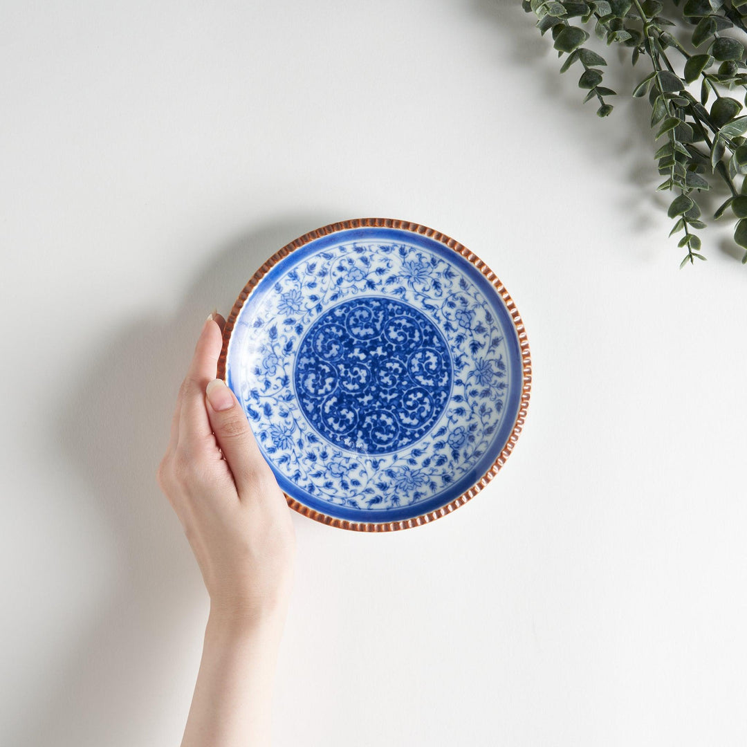 A ceramic plate with an intricate blue floral design centered around a bold circular pattern, framed by a copper-colored textured rim.