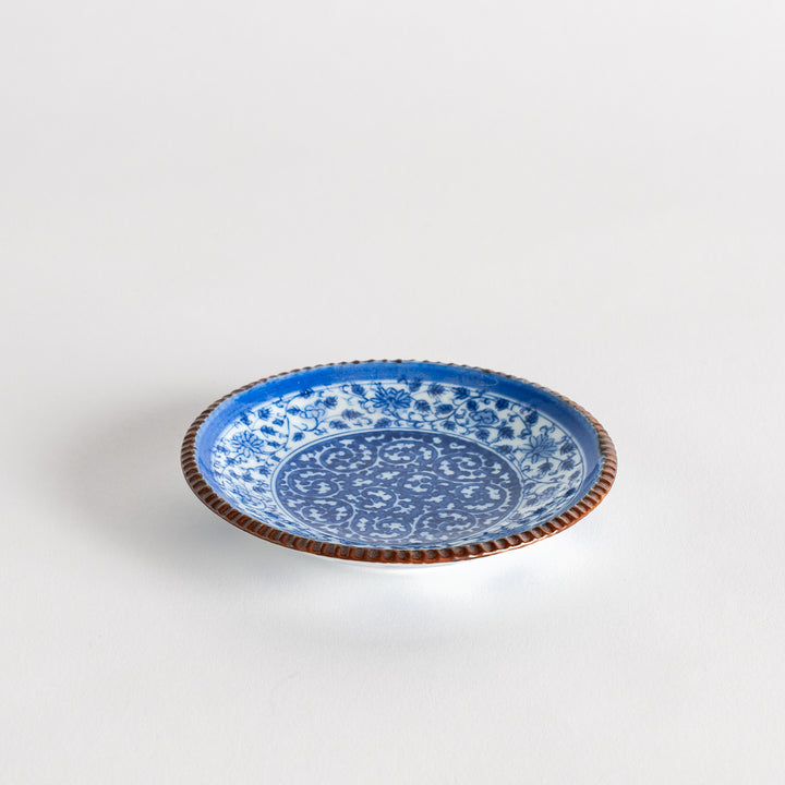 A small ceramic plate with an intricate blue floral design centered around a bold circular pattern, bordered by a copper-colored textured rim.