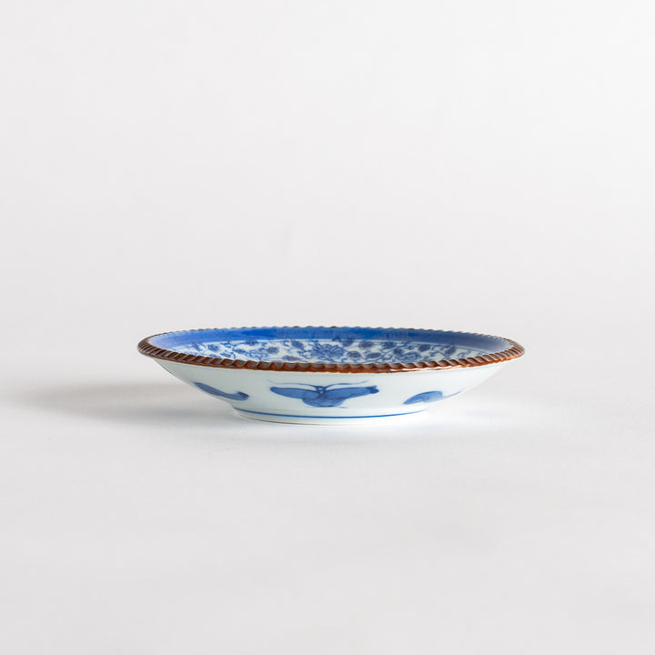 A small ceramic plate with an intricate blue floral design centered around a bold circular pattern, bordered by a copper-colored textured rim.