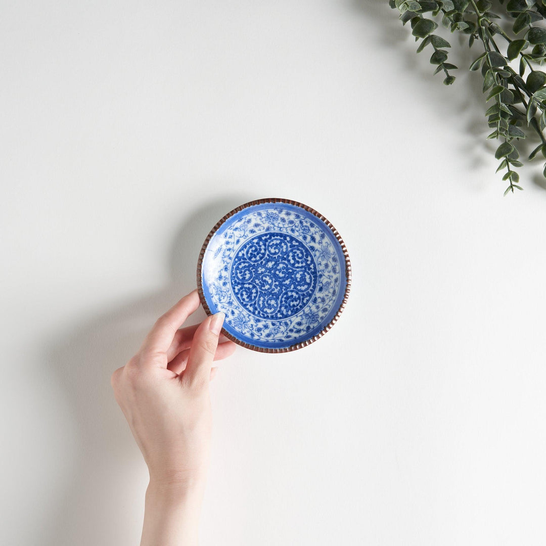 A small ceramic plate with an intricate blue floral design centered around a bold circular pattern, bordered by a copper-colored textured rim.