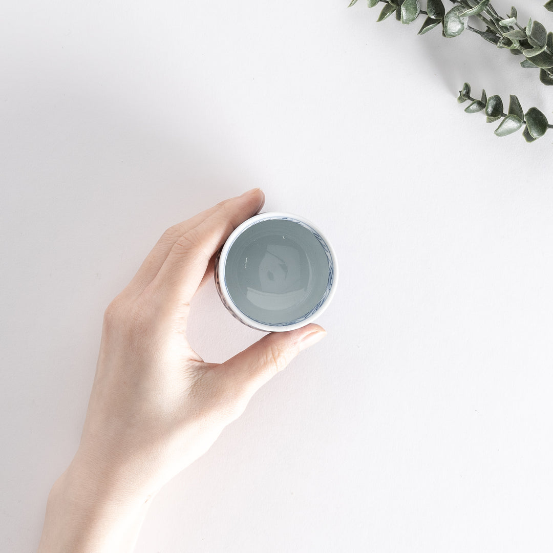 Top-down view of a sake cup held in hand, showcasing the detailed blue arabesque landscape design.