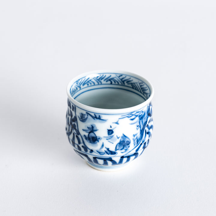 Diagonal view of the sake cup, highlighting the intricate blue arabesque landscape pattern with fish and waves.