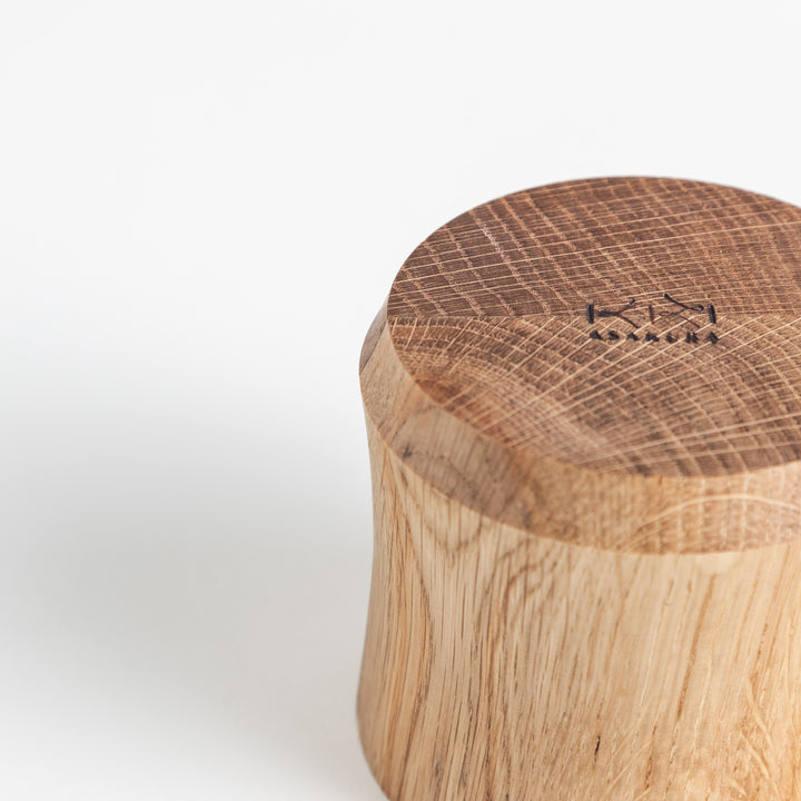 Side view of the wooden cup, showing the unique curving design and engraved brand mark on top.