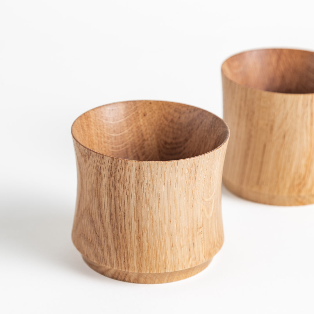 Close-up view of two Artisan Mizunara Oak whisky cups with smooth, natural wood finish and unique shaping at the base.