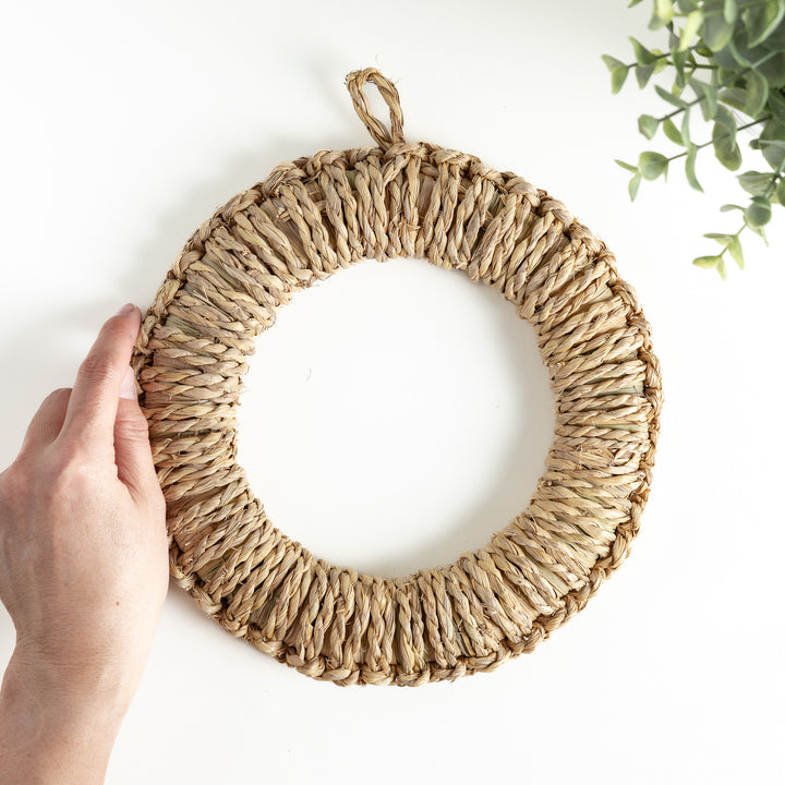 Handwoven rush trivet in large size, held by hand to showcase its texture and shape, featuring a loop for easy hanging.