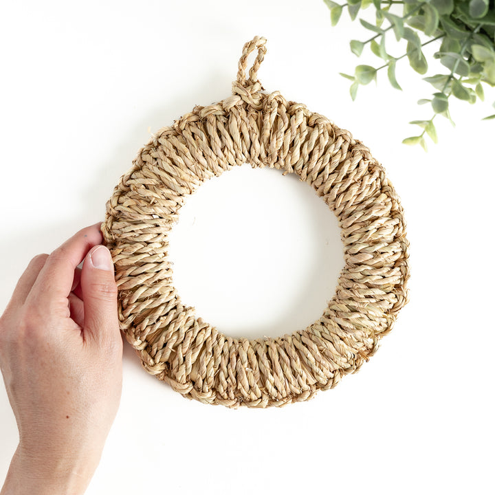 A hand holding a medium-sized straw trivet. Its woven texture and durable material are clearly visible, perfect for everyday use.