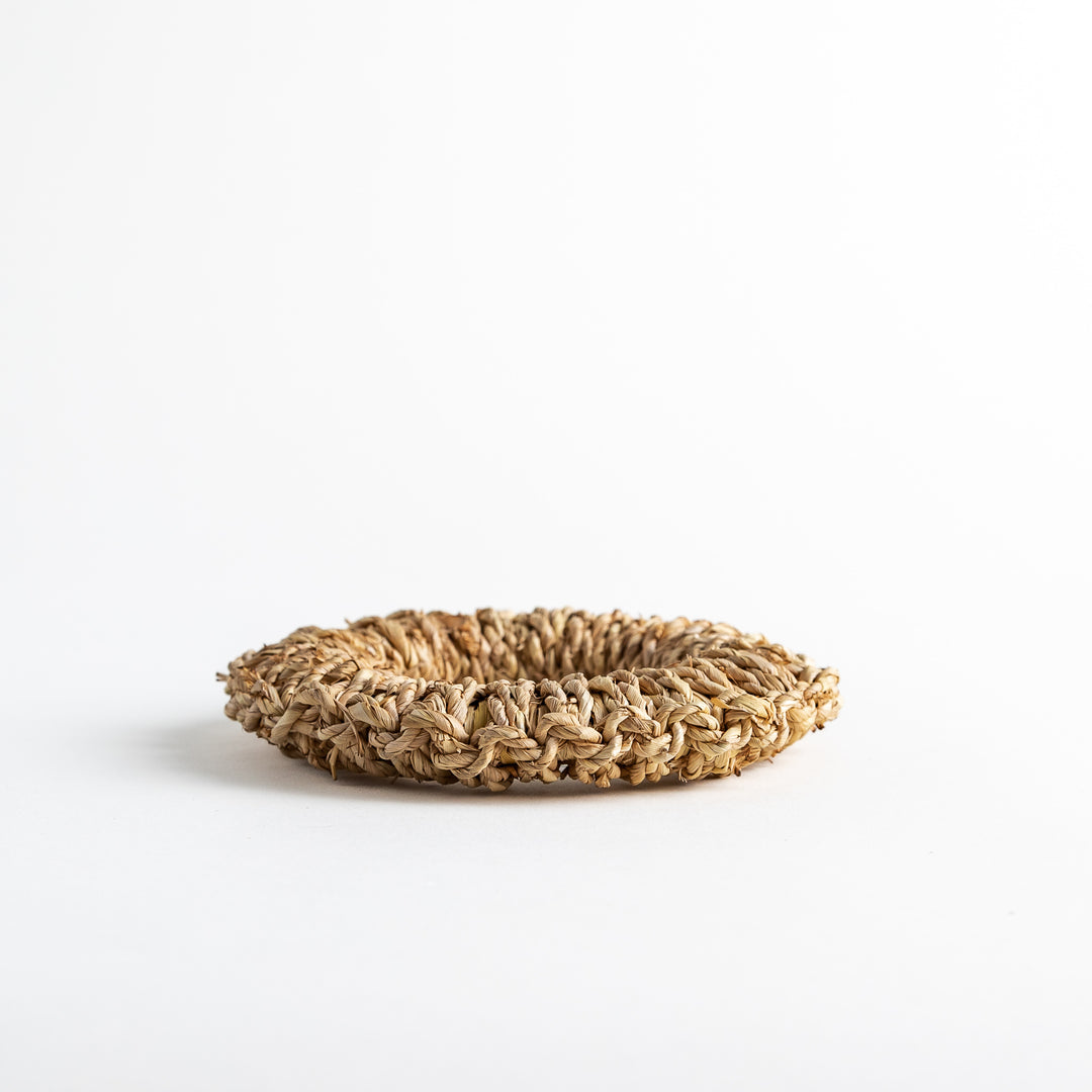 Low side view of a circular rush trivet, displaying its natural woven texture.