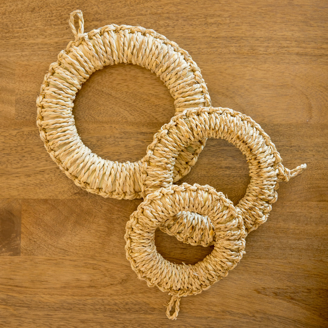 Three artisan rush trivets in varying sizes, neatly arranged on a wooden surface.