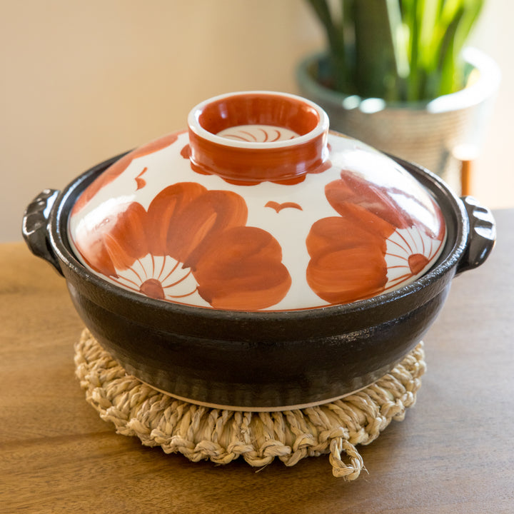 A donabe with a flower motif lid, placed on a large artisan rush trivet.