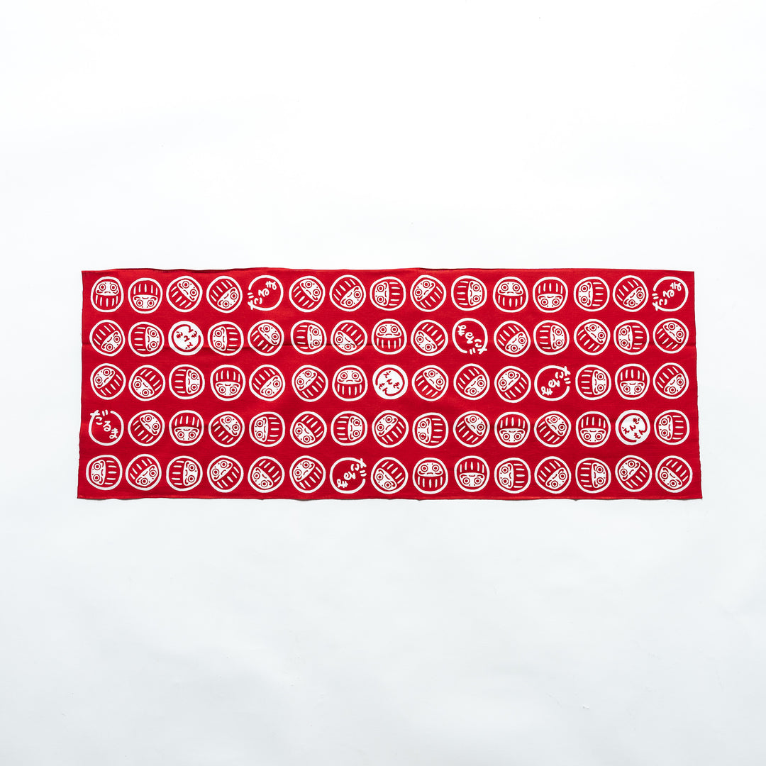 Fully spread-out red tenugui showcasing white Daruma patterns in a repeating design against a white background.