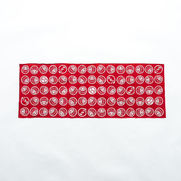 Fully spread-out red tenugui showcasing white Daruma patterns in a repeating design against a white background.