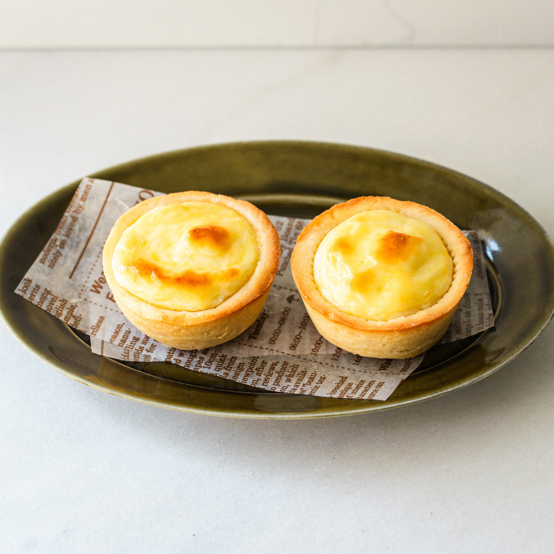 Top view of two baked cheese tarts with golden, slightly browned tops, placed on a green plate with parchment paper underneath.