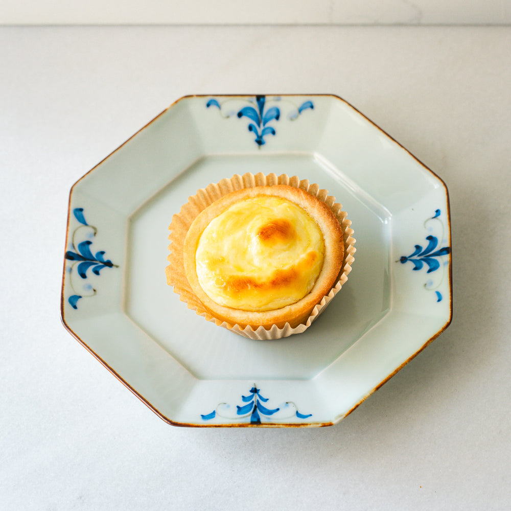 Top view of a baked cheese tart on an octagonal plate with blue floral patterns, showcasing the golden-brown top and pastry crust.