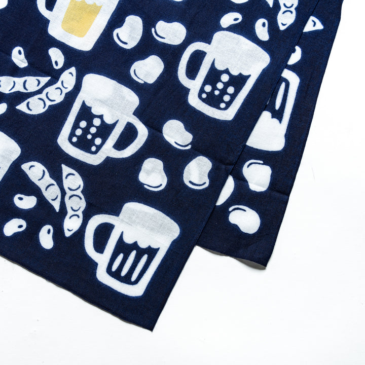 Close-up of beer mugs, soybeans, and edamame patterns on a dark navy tenugui, highlighting intricate white details.