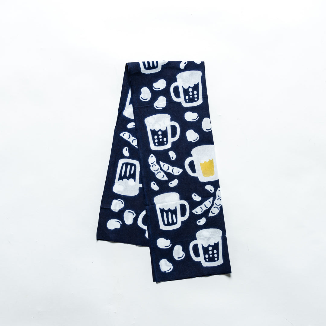 Dark navy tenugui with beer mugs, soybeans, and edamame pattern, neatly folded for display.