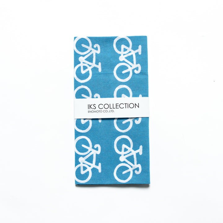 The blue tenugui is neatly folded, showcasing a product sleeve with the bicycle motif.