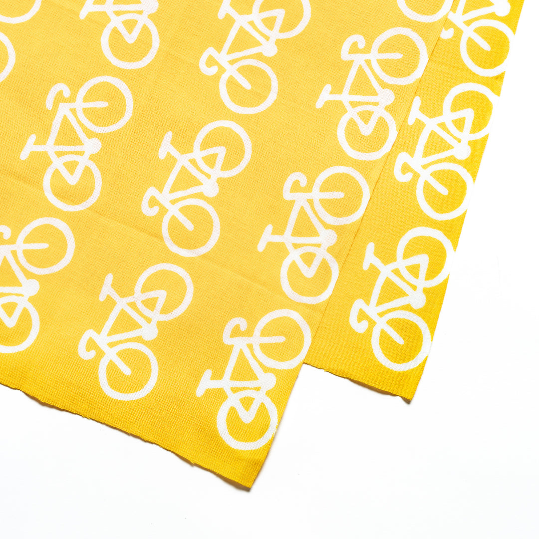 Close-up view of the white bicycle design on the bright yellow fabric.