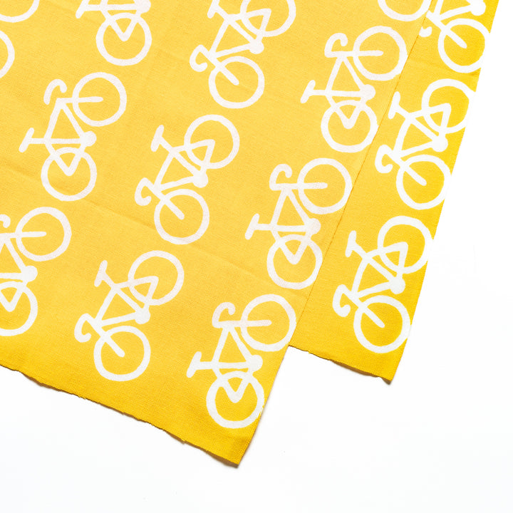 Close-up view of the white bicycle design on the bright yellow fabric.