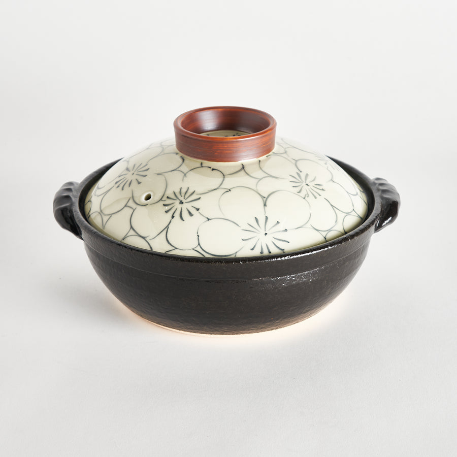 Black donabe with a cream-colored lid featuring black floral patterns and a brown ring on top.