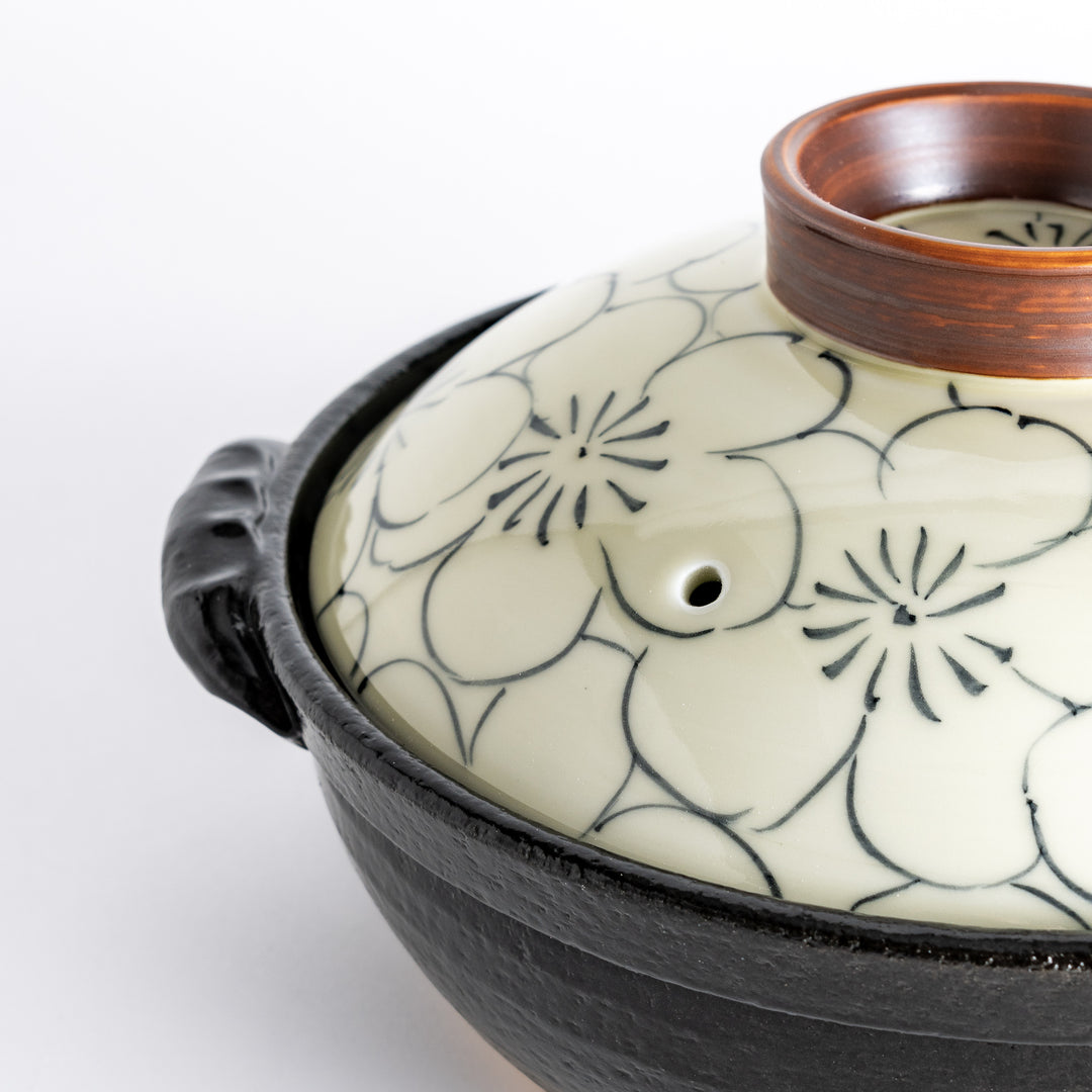 A 8-inch donabe with a vibrant black floral pattern lid and black pot.