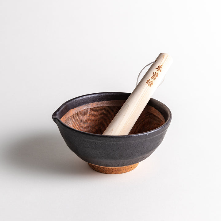 A black ceramic mortar with an elegant, ridged interior, paired with a wooden pestle for grinding.