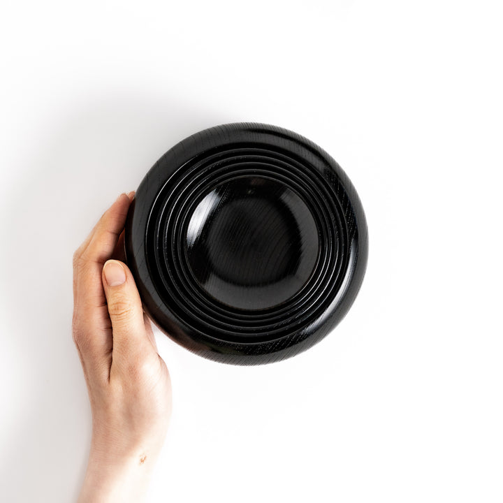 Hand-held black lacquered Oryoki bowl showcasing a smooth, glossy finish and a nested base design with concentric grooves for stability.