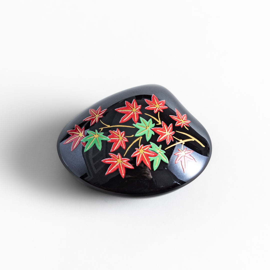 Black ceramic incense holder shaped like a seashell, adorned with red and green maple leaves, featuring a glossy red incense stand inside for secure placement.