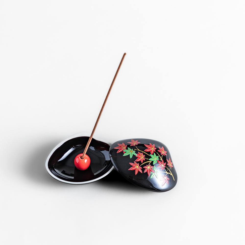 Black ceramic incense holder shaped like a seashell, adorned with red and green maple leaves, featuring a glossy red incense stand inside for secure placement.