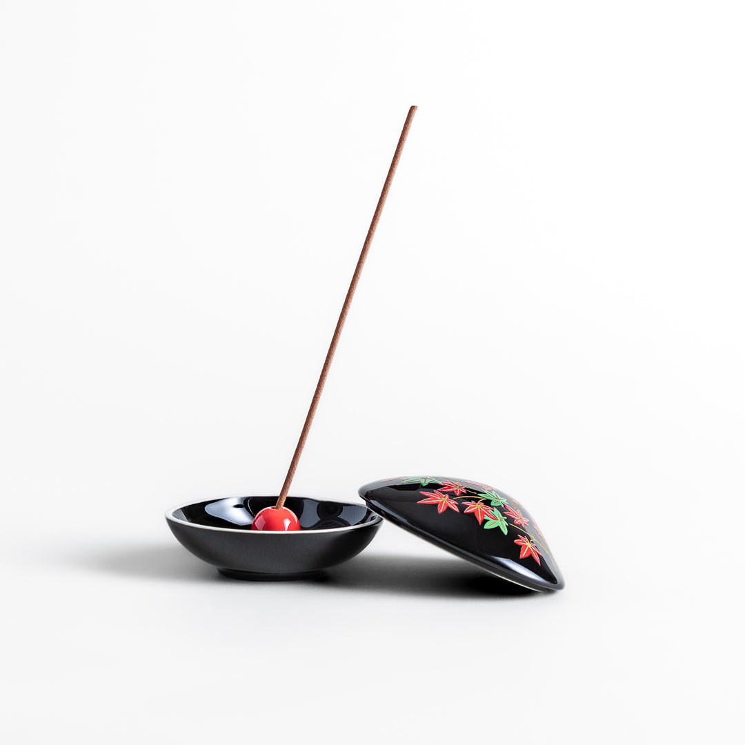 Black ceramic incense holder shaped like a seashell, adorned with red and green maple leaves, featuring a glossy red incense stand inside for secure placement.