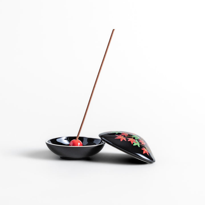 Black ceramic incense holder shaped like a seashell, adorned with red and green maple leaves, featuring a glossy red incense stand inside for secure placement.