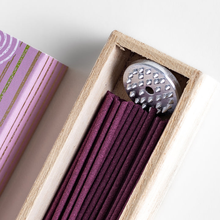 Incense in a light wooden box with rich purple sticks, presented in elegant packaging featuring white circular patterns on a soft lavender background for a serene ambiance.