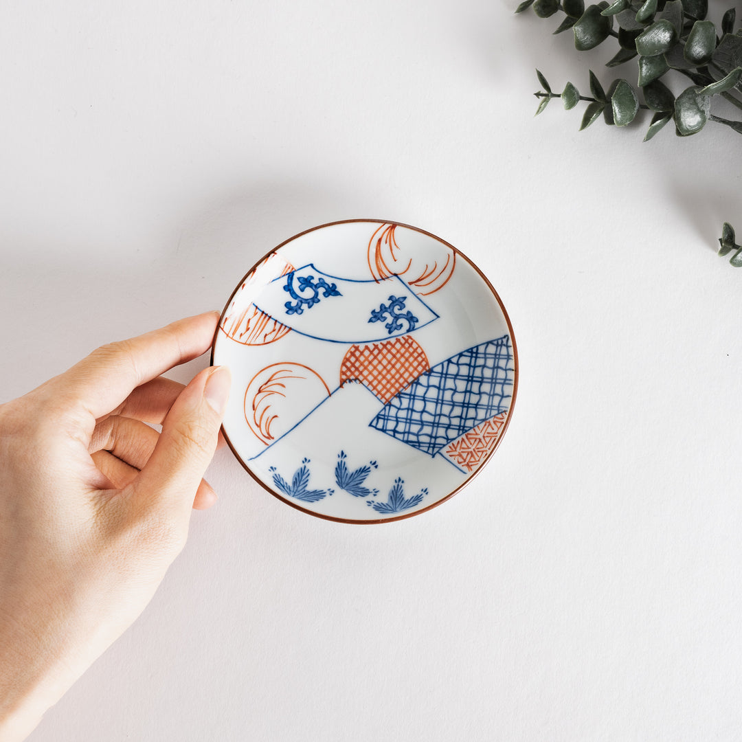 Hand holding a sauce dish with a blue fan pattern and Mount Fuji design, highlighting its artistic features against a light background.