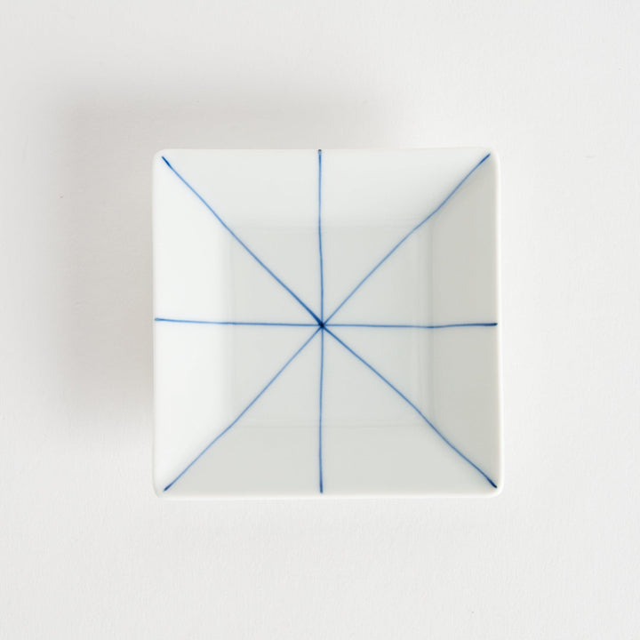 Top view of a square white sauce dish with a blue line pattern, placed on a light surface.