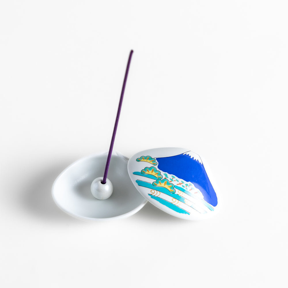 White ceramic incense holder shaped like a seashell, featuring a vivid blue Mount Fuji design with golden accents and a secure incense stand inside for elegant display.