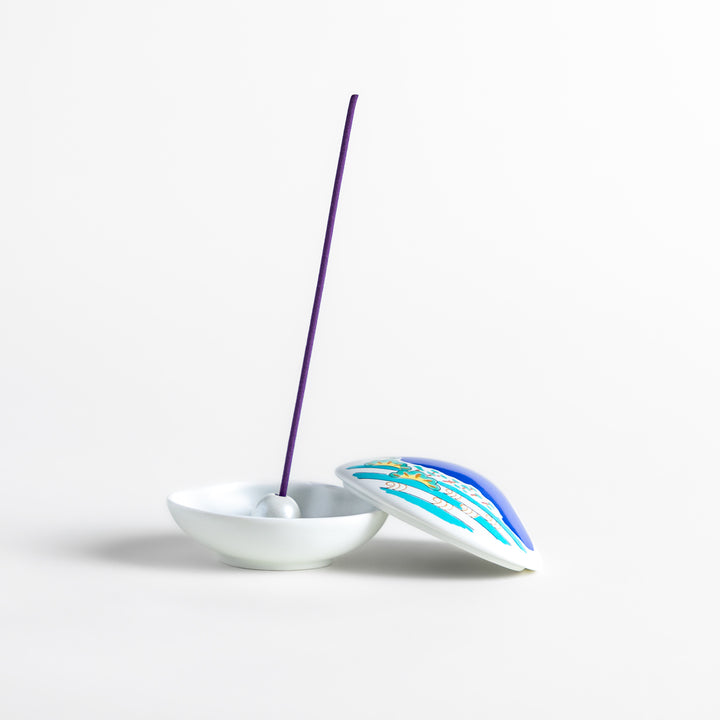 White ceramic incense holder shaped like a seashell, featuring a vivid blue Mount Fuji design with golden accents and a secure incense stand inside for elegant display.