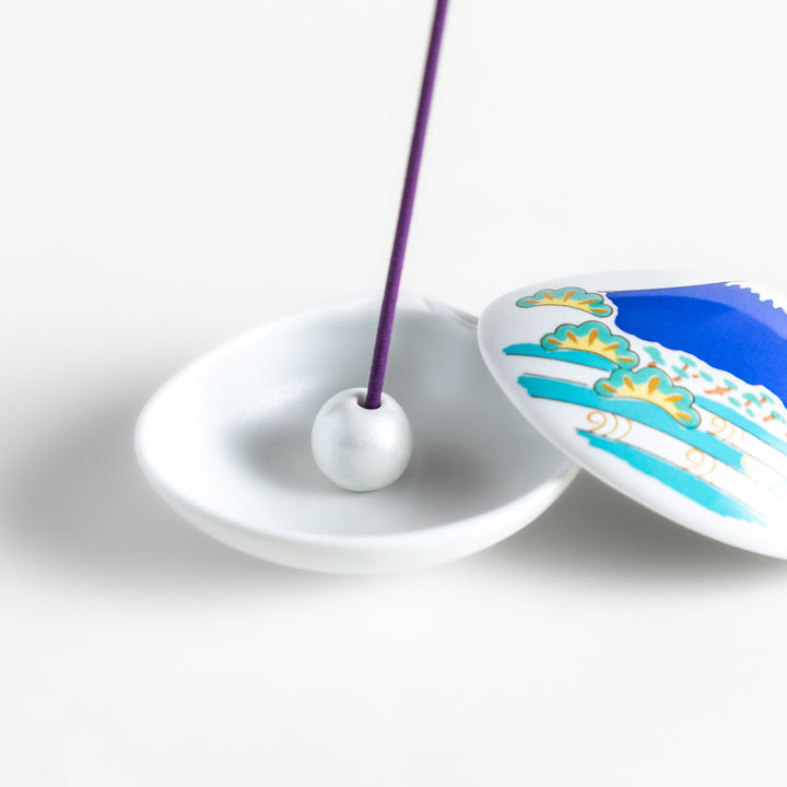 White ceramic incense holder shaped like a seashell, featuring a vivid blue Mount Fuji design with golden accents and a secure incense stand inside for elegant display.