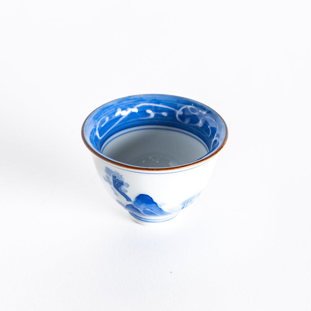 Slightly angled view of a blue and white porcelain sake cup, highlighting the elegant curves and mountain design.