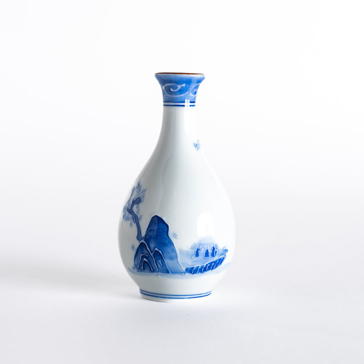 A blue and white sake flask with elegant hand-painted mountain and tree motifs on a smooth porcelain body.