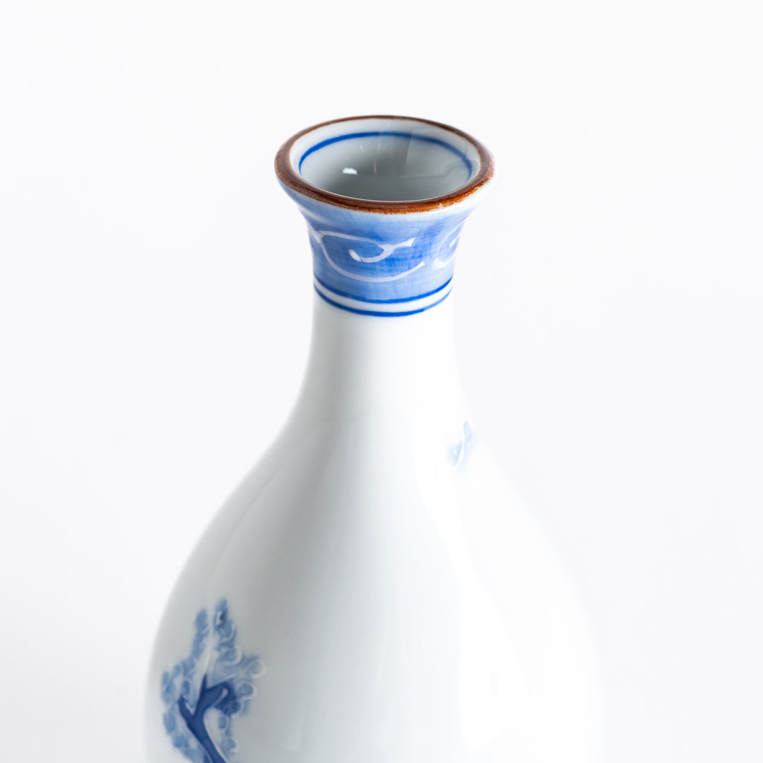 Close-up of the hand-painted blue mountain and tree motifs on the smooth white porcelain surface of the sake flask.