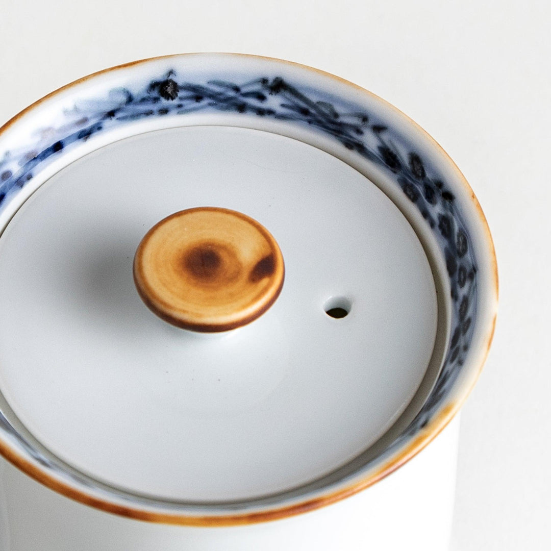 A small white ceramic soy sauce dispenser with a blue floral pattern along the rim.