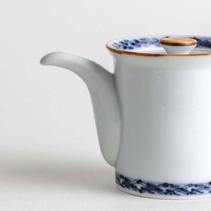 A small white ceramic soy sauce dispenser with a blue floral pattern along the rim.