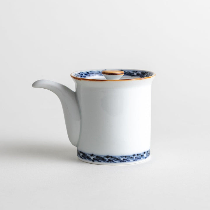 A small white ceramic soy sauce dispenser with a blue floral pattern along the rim.